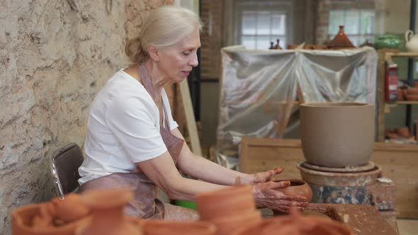 Senior Female Potter Ceramist Working on Pottery Wheel While Sitting in Her Workshop