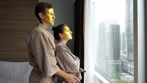 Man Hugs Girl with Golden Face Mask Near Window in Hotel