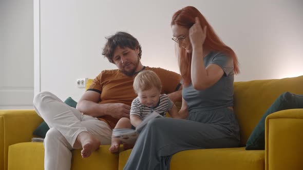Family Sitting on Yellow Couch and Teaching the Baby How to Read  the Baby Drawing in a Book