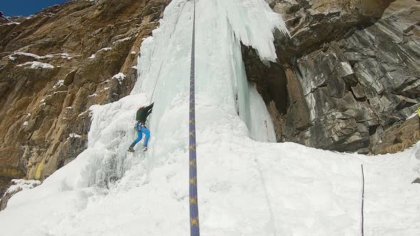 Man Climbing Ice Waterfall with Rope and Ice Axe