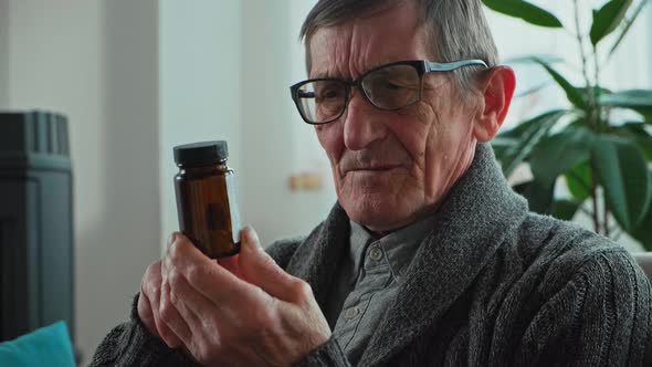 Elderly Senior in Eyeglasses Holding a Bottle of Pills in Hands for the Treatment of Visual