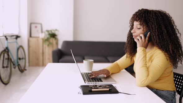 Young Woman Using Mobile Phone While Working on Laptop at Home Office alt