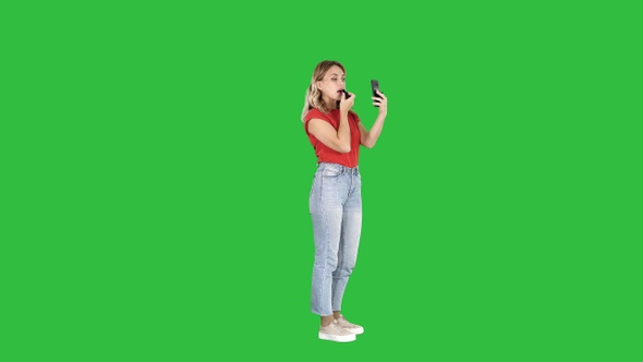 Woman using lipstick and looking in her phone on a Green