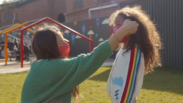Side View of Caucasian Mother Putting Safety Mask on African Daughter Face Outdoors