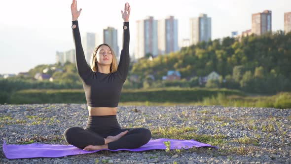 Young Sporty Woman Sits Relaxed on a Mat with Hands Together, Meditation