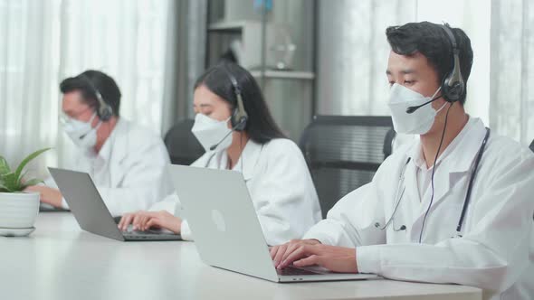 Three Asian Doctors With Stethoscopes Wearing Headsets And Masks Working As Call Centre Agents