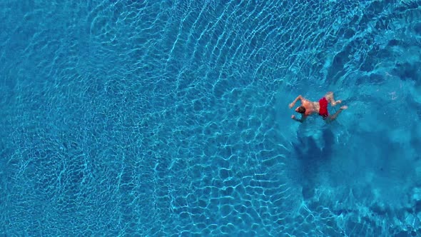 Aerial View of Man in Red Shorts Swims in the Pool