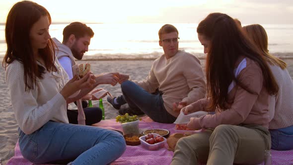 Happy Friends Eating Sandwiches at Picnic on Beach