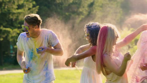 Cheerful Young Woman Throwing Holi Colors at Boyfriend, Friends Having Fun