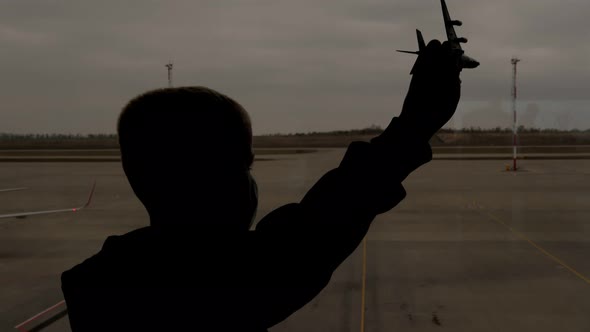 Silhouette of a Boy in a Medical Mask at the Airport with a Toy Airplane