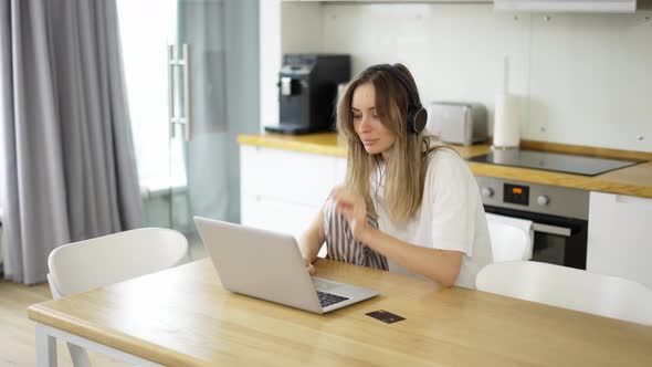 Woman in Headphones at Kitchen Listening to Music and Makes an Online Purchase Using a Credit Card