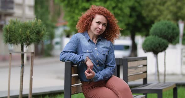 Attractive Young Ginger Woman Sitting on a Bench Looking Away and at the Camera, Beautiful Face