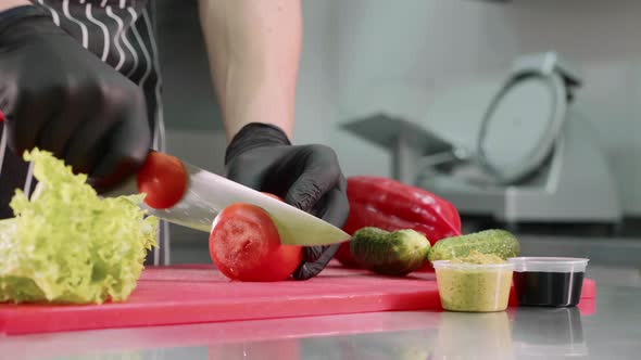Chef is cutting tomato for burger, hands in black gloves closeup.