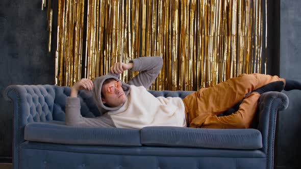 Stylish Man in Hoodie with Ears and Sunglasses Lying on Sofa
