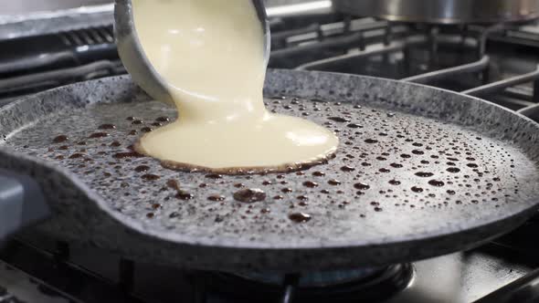 Ladle spoon pours pancake batter on hot oil on pan, hotcake breakfast, close up