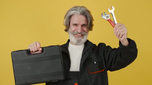 Stylish Senior Handyman Shows Tools on Yellow Background