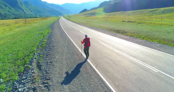 Flight Over Hitchhiker Tourist Walking on Asphalt Road. Huge Rural Valley at Summer Day. Backpack