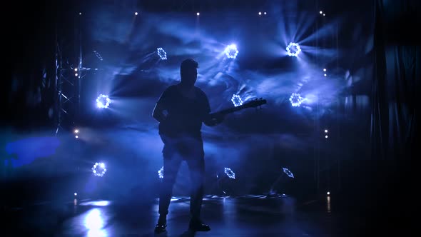 Silhouette of a Young Guy Playing on the Electric Guitar on Stage in a Dark Studio with Smoke and