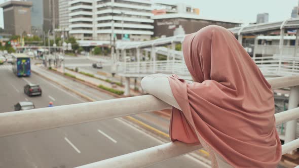 A Young, Sad Muslim Girl Stands on a Bridge Over Road Traffic in Downtown Jakarta