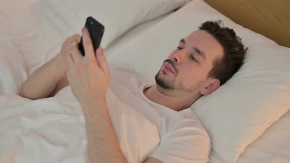 Young Man Celebrating Success on Smartphone in Bed