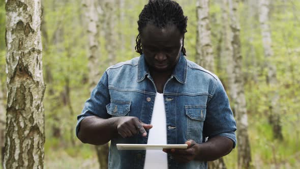 African Man Using the Tablet in the Nature. Touching the Screen. Slow Motion