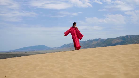 Sexy Brunette Woman in a Red Satin Long Dress Walks on Sand Dunes in the Desert