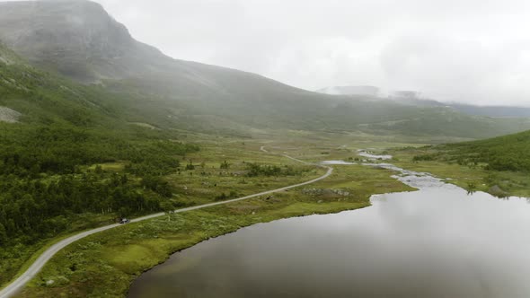 A Car Travelling Along The Road Near The Calm Lake And Mountain Range Of Hemsedal, Norway. - Aerial