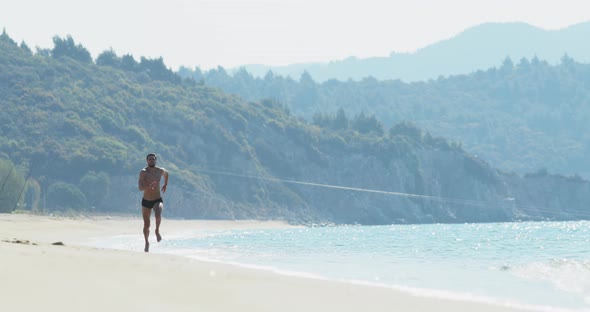 The Handsome Man with a Perfect Athletic Body in Swimming Trunks Having Fun on a Deserted Beach in