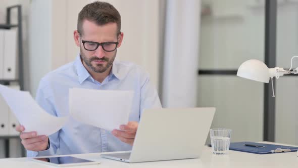 Middle Aged Man Having Loss on Documents While Working on Laptop