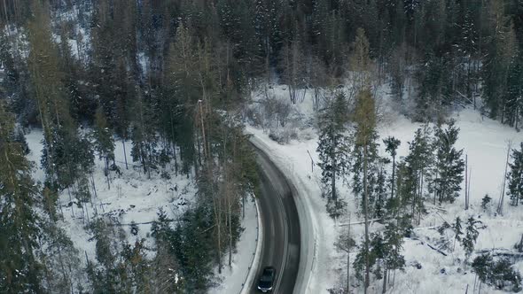 Car driving on frozen mountain road in winter season. Aerial backward
