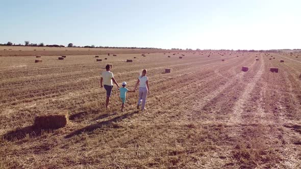 Happy Family Walks Into a Field Holding Their Son's Hands