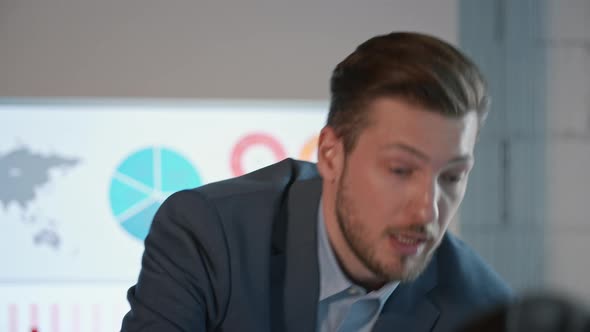 Young man in a suit telling his colleagues about financial strategy on the background of infographic