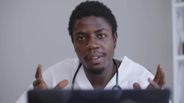 Closeup Portrait Serious Intelligent African American Doctor Sitting at Laptop Talking and Gesturing