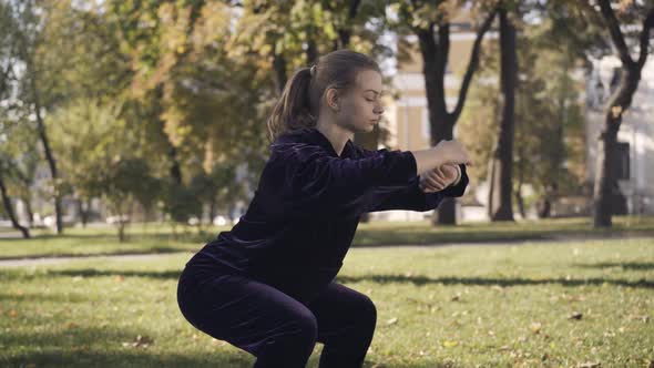 Concentrated Sportswoman Standing in Squat and Checking Time on Watch