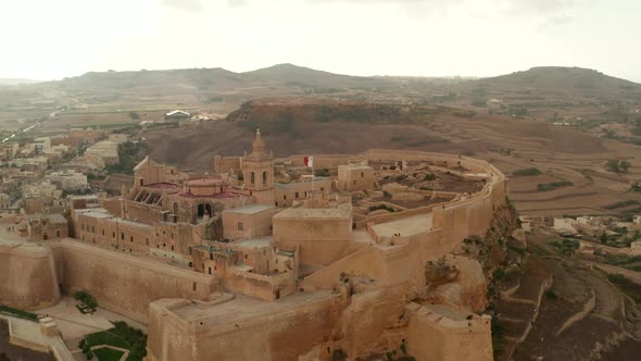 Establishing Shot of Gozo Castle Fort with Malta Flag Waving Castle in Beautiful Sand Brown Color