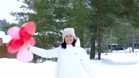 Happy woman throws up heart-shaped balloons outdoor in winter with snow