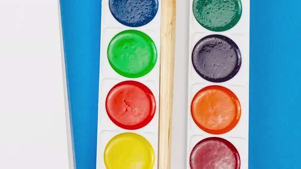 Multicolored Colorful Paints with a Wooden Brush Lie on a Pastel Blue Background