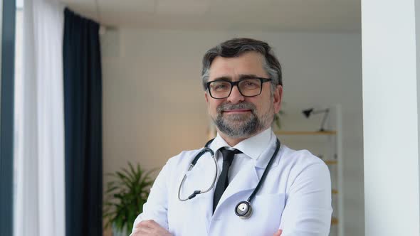 Cheerful Senior Physician in White Suit with Arms Crossed and Stethoscope