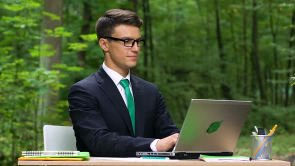 Young Smiling Office Worker Typing on Laptop Sitting in Green Park, Slow-Mo