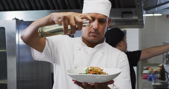 Caucasian male chef garnishing dish and smiling in restaurant kitchen