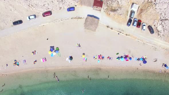 Flying above parked cars and people on sandy beach of Pag island