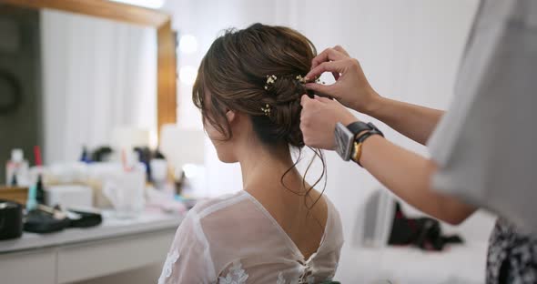 Female hairdresser standing and making hairstyle on bride in beauty salon