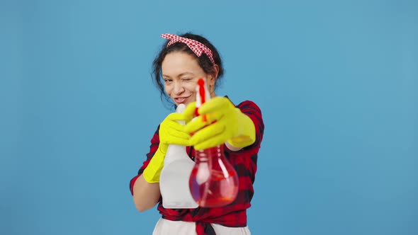 Happy Cleaning Lady Dancing with Spray Detergents and Smiling to Camera Blue Background