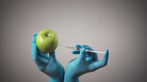 Female Hands in Medical Gloves Making Injection in Apple. Healthy and Unhealthy Eating, GMO Products