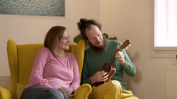 Man playing the ukulele to pregnant wife at the living room.