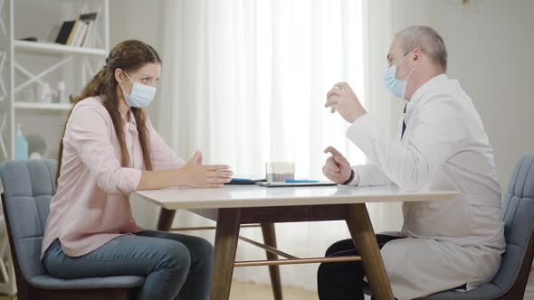 Mid-adult Psychologist in Face Mask Offering Pills To Young Stressed Woman on Covid-19 Pandemic