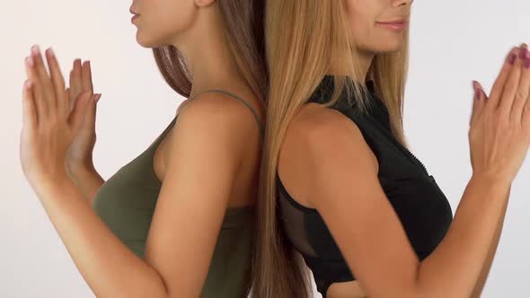 Two Women Standing Back To Back Putting Hands Into Meditation Position