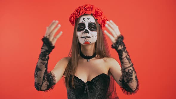 Day of Dead Woman with Sugar Skull Makeup is Smiling and Looking at you Posing on Red Background