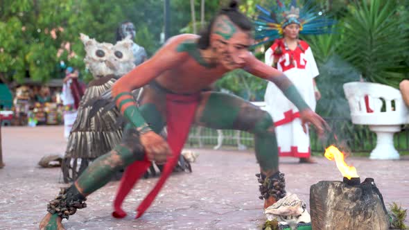 Closeup of Mayan or Aztec fire dancer in with a person in bird costume with feathers behind in Mexic