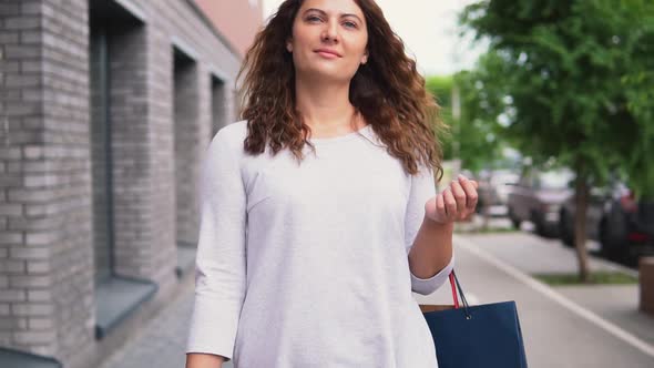 A Girl in a Light Dress with Long Hair Goes Down the Street After Shopping Having a Good Mood and